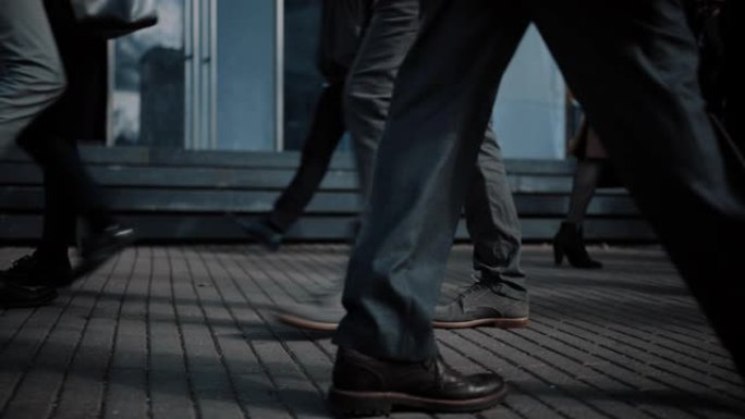 一个商务人士步行通勤到办公室的特写镜头。经理和商人走在拥挤的步行街上。人们穿得很聪明。冷光。