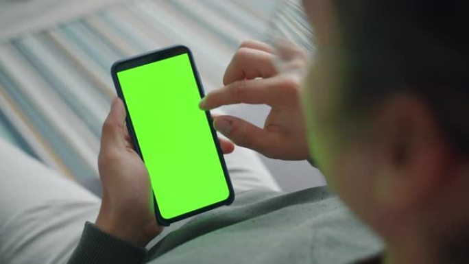 一个人独自坐在家里拿着绿屏色度键智能手机的特写
