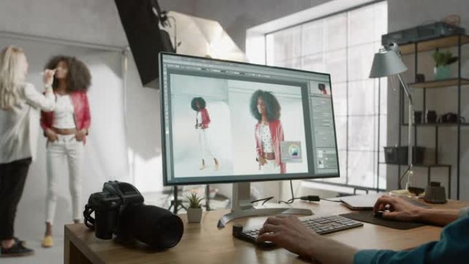 坐在办公桌前的专业摄影师在照相馆润饰中使用台式计算机。拍摄后，他在图像编辑软件中修饰了美丽的黑人女性