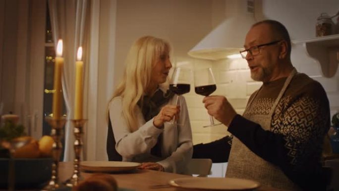 恋爱中的幸福高级夫妇在浪漫的晚餐上互相敬酒，在厨房里吃美味的饭菜，庆祝周年纪念日。年老可爱的夫妻有浪
