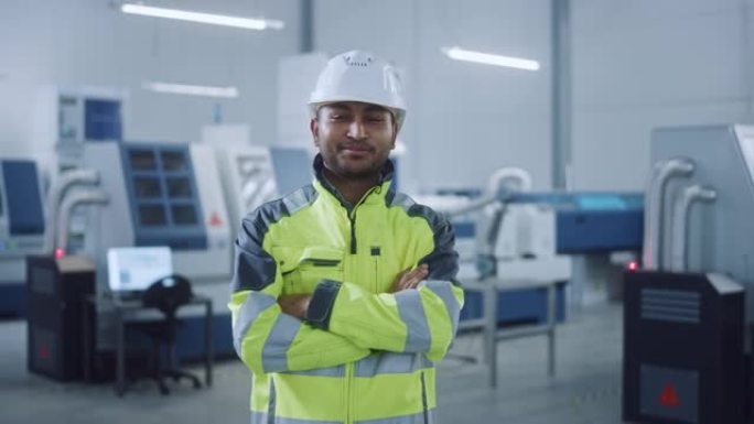 穿着安全背心和安全帽的英俊印度工程师的肖像交叉双臂微笑。在现代制造工厂工作的职业女性。具有数控机械和