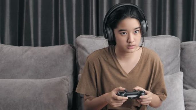 4k分辨率迷人的亚洲女孩戴着无线耳机拿着操纵杆或游戏控制器，在家玩在线视频游戏机。孩子喜欢在冠状病毒