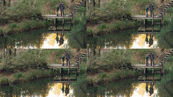 小男孩正在学习从父亲那里一起站在木墩上，拿着钓鱼竿说话。美丽的湖泊和森林是可见的。