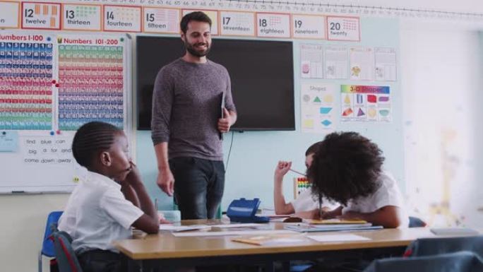带有数字平板电脑的男老师在学校教室里教一群穿制服的小学生