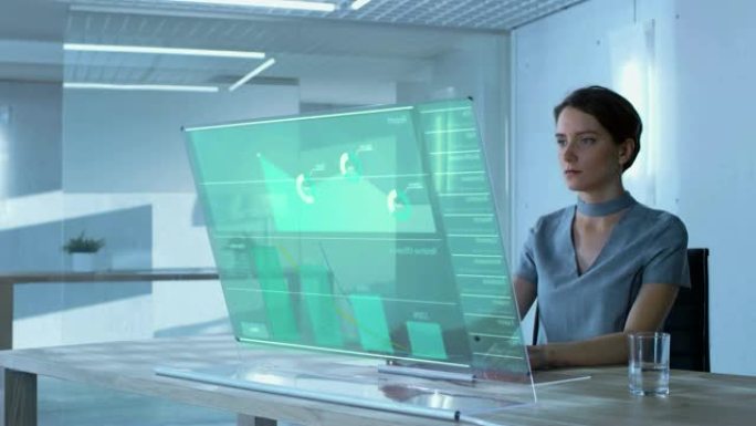 未来派概念: 在办公室里，漂亮的女性计算机科学家在透明的计算机显示屏上与触摸屏键盘一起工作。屏幕显示