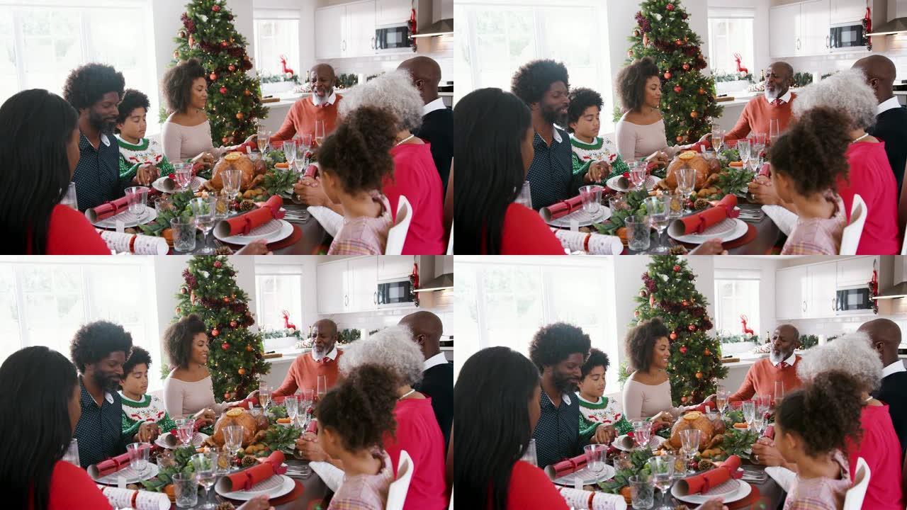 多代混血家庭坐在圣诞餐桌上手牵手说着优雅，选择性聚焦