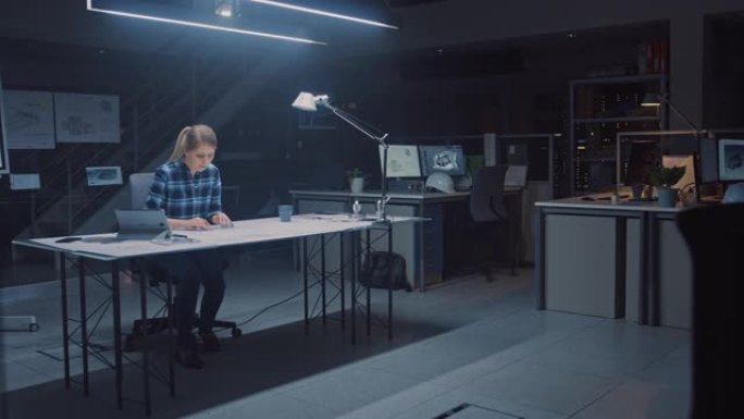 坐在办公桌前的女工程师将蓝图放在桌子上，使用铅笔，尺子和数字平板电脑，并喝咖啡。在黑暗的工业设计工程
