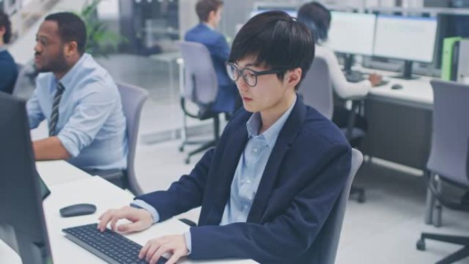 年轻的专业日本股票经纪人庆祝交易成功。在现代开放式办公室中，多元化且积极进取的商人在计算机上工作。