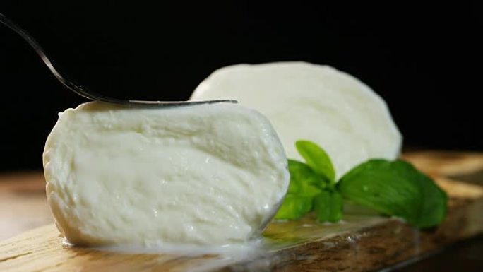 宏观拍摄新鲜的意大利马苏里拉奶酪和充满牛奶的生物，背景是红色西红柿和罗勒。