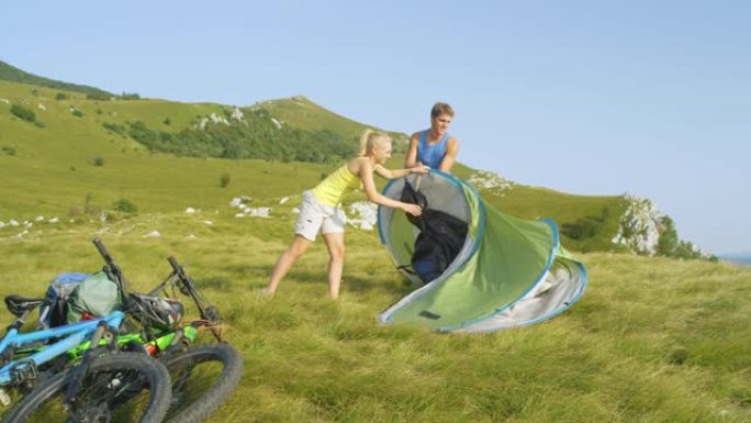 慢动作开朗的活跃夫妇在山上的草地上搭帐篷