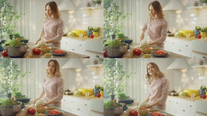 穿着条纹套头衫的年轻女性正在现代阳光明媚的厨房里制作健康的有机沙拉。正宗的女人正在用刀切碎花椰菜。她