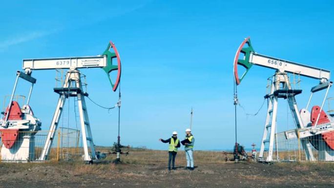 石油开采现场，两名工程师在他们之间进行沟通。能源、石油、天然气、燃料泵送钻机。