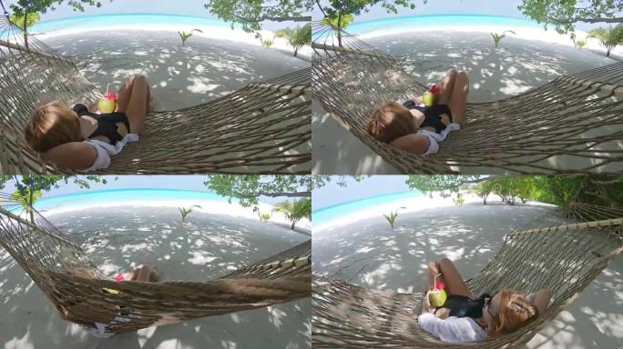 女士在马尔代夫热带海洋海滩的吊床上喝椰子饮料