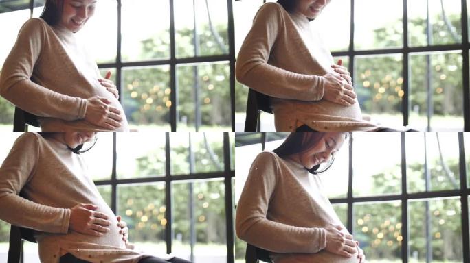 亚洲孕妇透过窗户看，在家揉肚子