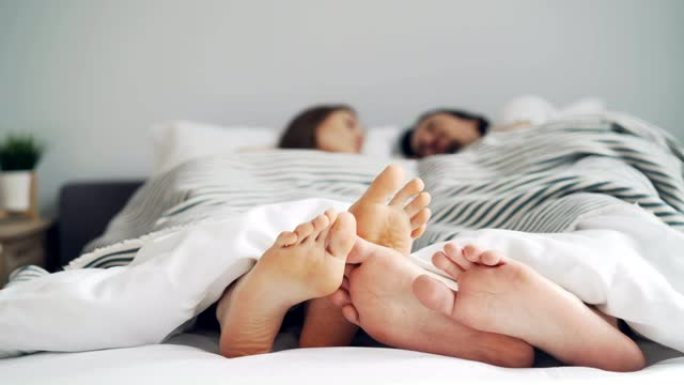 当人们躺在一起时，女孩和男孩的脚在毯子下的床上触摸