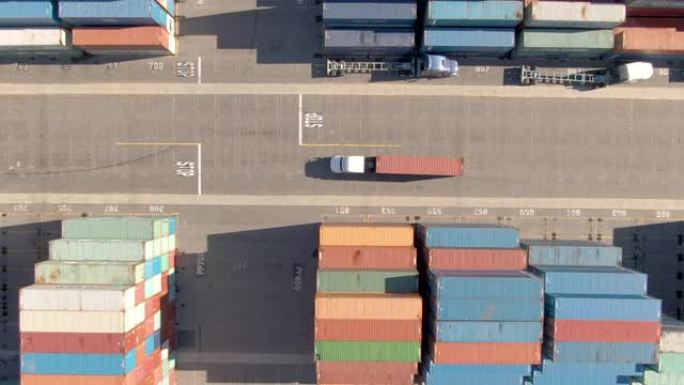 自上而下: 白色卡车在繁忙的港口运送一个红色的货运集装箱。