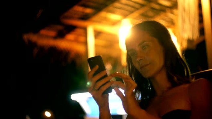 使用智能手机电子商务应用程序在线在night lounge beach cafe中拍摄快乐轻松的年轻