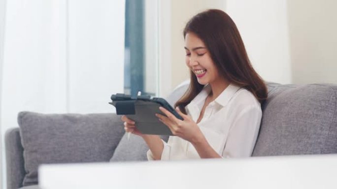 年轻的亚洲商务女性在起居室使用平板电脑视频通话与家人通话。