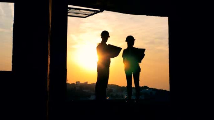 站在多层建筑，建筑工地中的男性和女性工程师的剪影