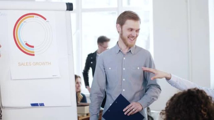 年轻的专业微笑的高加索商人在办公室会议销售图表上激励快乐的公司员工。