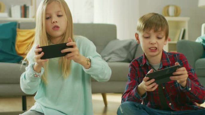 在家坐在地毯上: 可爱的小女孩和可爱的男孩在两部智能手机上玩竞争性视频游戏，将它们保持在水平景观模式