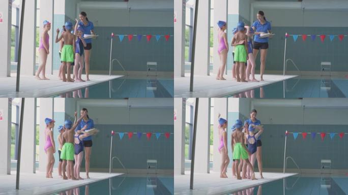 女教练站在室内游泳池边缘时，在游泳课上给孩子们指导
