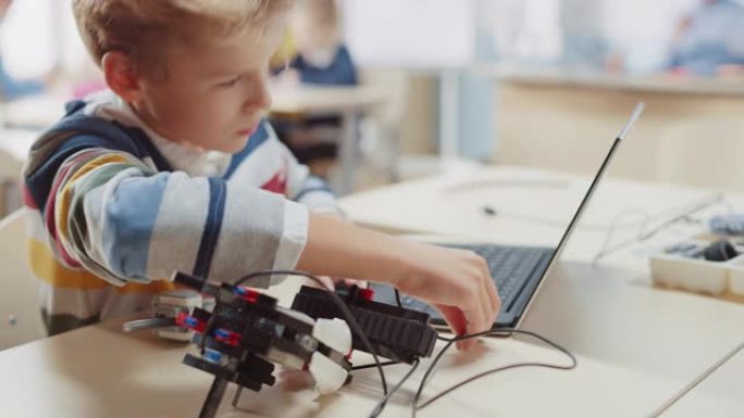 小学生将电缆连接到小型机器人，使用笔记本电脑为机器人工程课程编程软件。小学科学教室，有天才的才华横溢