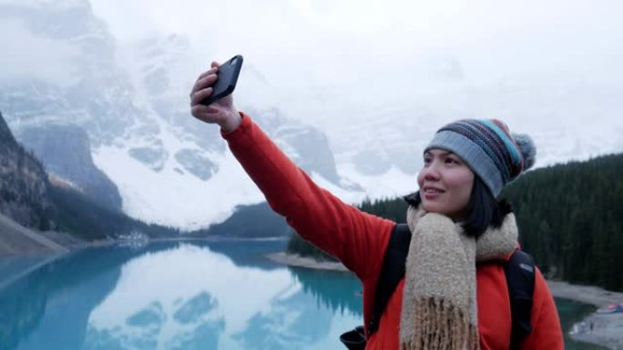 年轻的女旅行者在加拿大艾伯塔省的冰碛湖用智能手机拍照