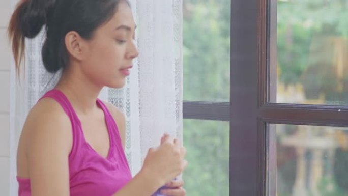年轻的亚洲女性喝水，因为在客厅里运动后感到疲惫的休息，迷人的美丽女性在家中锻炼身体。女人在家锻炼的概