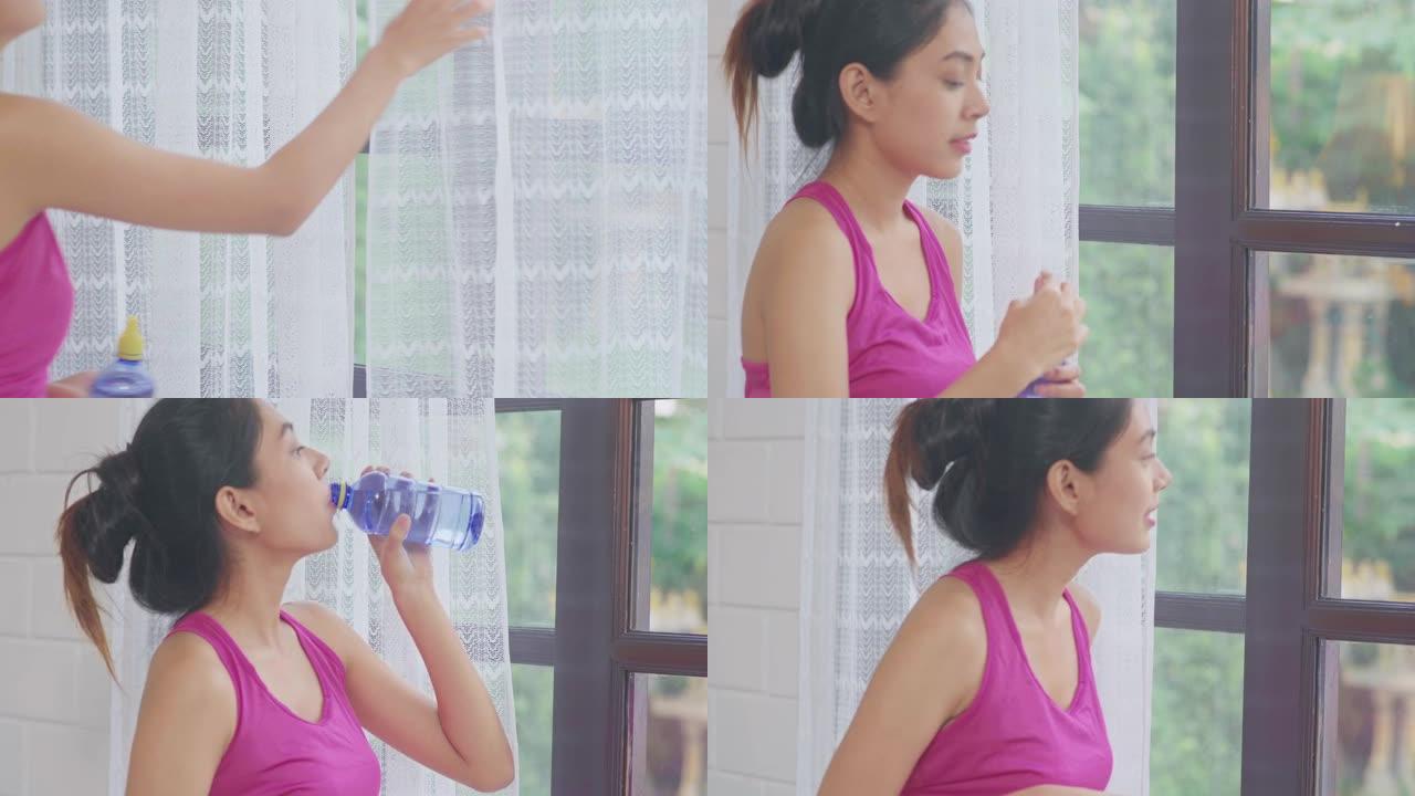 年轻的亚洲女性喝水，因为在客厅里运动后感到疲惫的休息，迷人的美丽女性在家中锻炼身体。女人在家锻炼的概