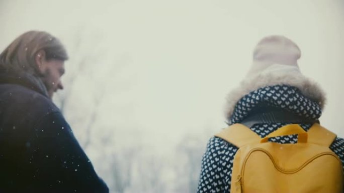 在寒冷的下雪天，快乐轻松的年轻男女带着明亮的黄色背包一起手牵着手行走。