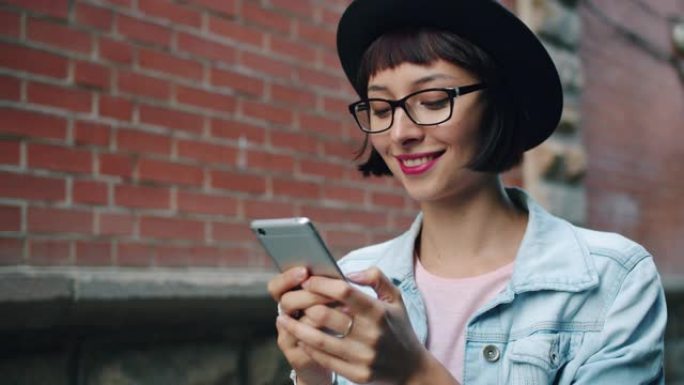 快乐女人的慢动作使用现代智能手机在城市户外行走