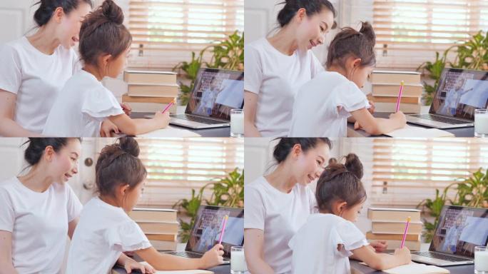 亚洲女儿年龄6-7岁与年轻妈妈在家学习在线课程。年轻的父母母亲教学校的女孩帮助坐在家里的桌子上学习家