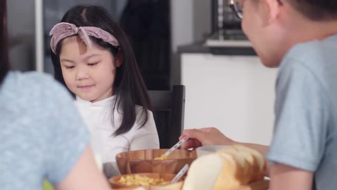 亚洲日本家庭在家里吃早餐。早上在厨房的桌子上吃面包，玉米片谷物和牛奶时，亚洲妈妈，爸爸和女儿在一起聊
