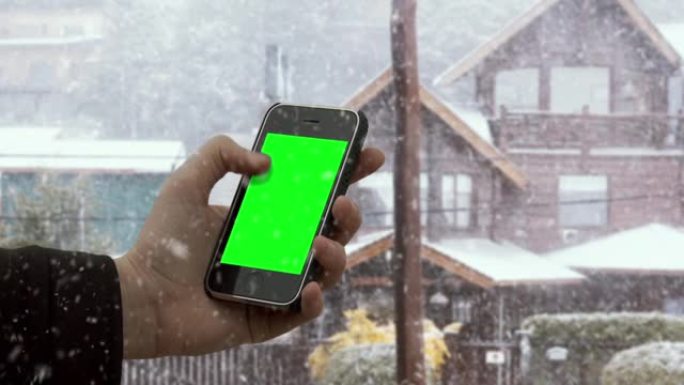 男性双手在白雪皑皑的背景下握着智能手机绿屏。