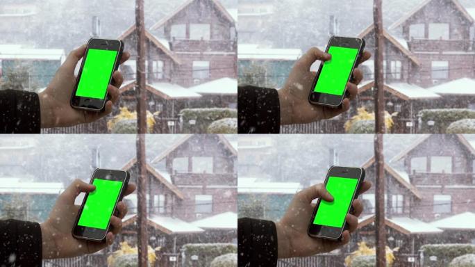 男性双手在白雪皑皑的背景下握着智能手机绿屏。