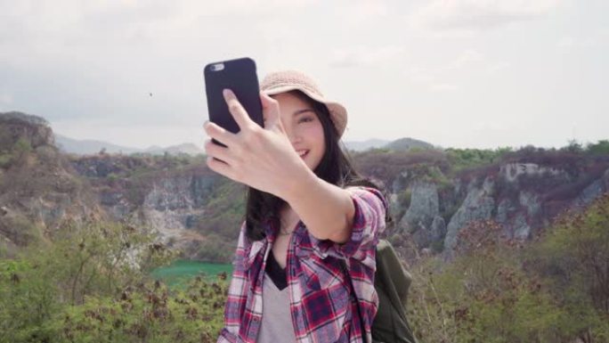 亚洲背包客女人在山顶上自拍，年轻女性快乐地用手机自拍享受假期徒步旅行冒险。生活方式女性旅行和放松概念