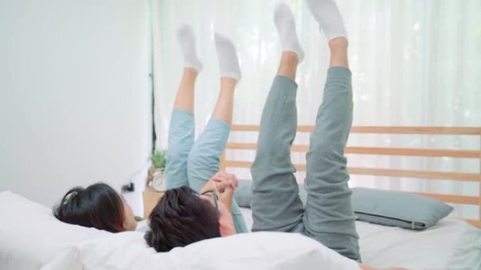 年轻的亚洲夫妇在床上一起玩耍，而早上在床上醒来。