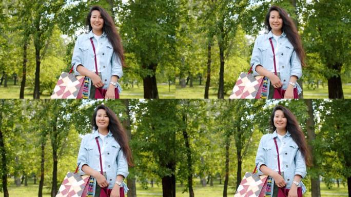 站在公园里带着购物袋微笑的漂亮亚洲女孩的肖像