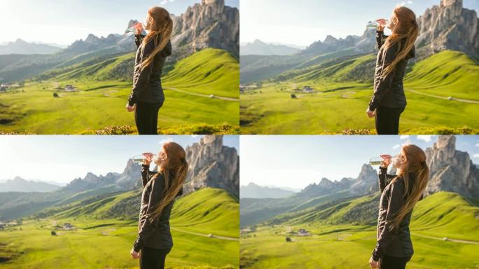 女人站在山顶俯瞰山谷，用可重复使用的水瓶喝水
