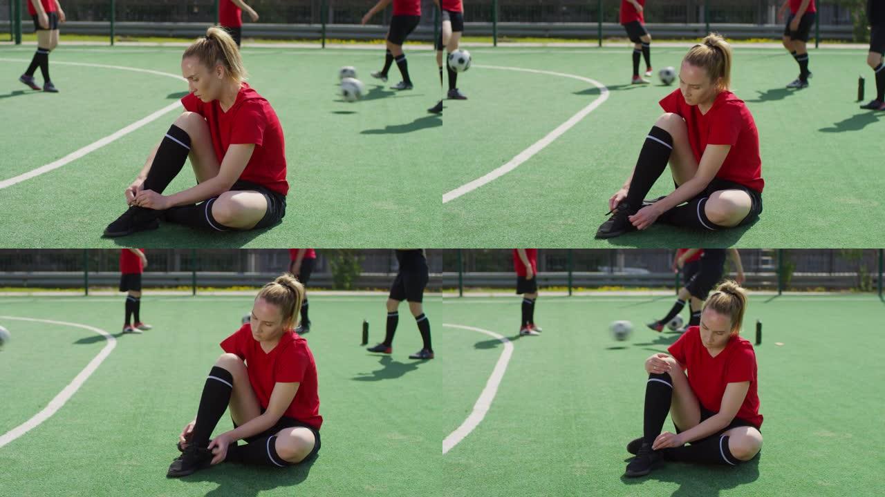 女足球运动员坐在球场上系鞋带