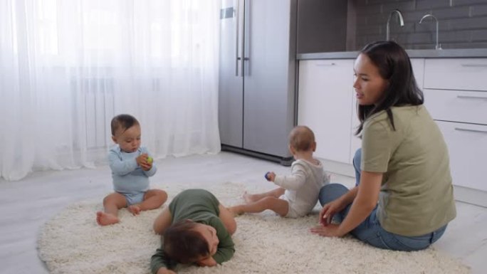 快乐的亚洲女人带着婴儿三胞胎在地毯上放松