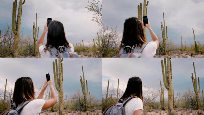 慢动作快乐的年轻成年旅游女子在亚利桑那州国家公园拍摄巨大的仙人掌仙人掌的智能手机照片。