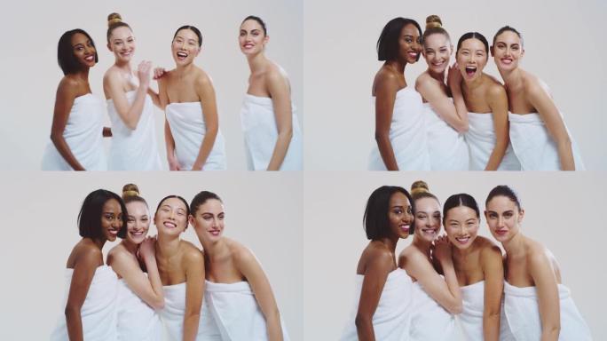 不同种族的美丽年轻女性的慢动作，完美结实苗条的身体，穿着白色浴巾，在相机里玩乐大笑，孤立在白色背景上
