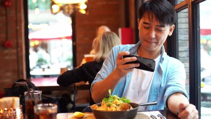 年轻的亚洲男子用智能手机拍摄食物照片