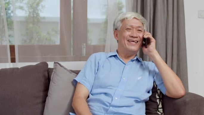 亚洲资深人士在家打电话。亚洲老年中国男性在家中躺在沙发上时，使用手机与家庭孙子们交谈。