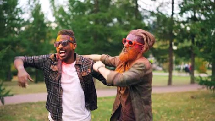 两个留着胡须的家伙，脸上满是油漆，在公园的草坪上跳舞，跳跃和微笑着享受派对。发型很酷的男人戴着墨镜。