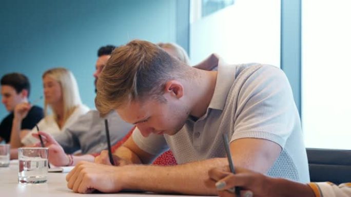 一群年轻候选人坐在会议室的桌子上，在商业毕业生招聘评估日做笔记