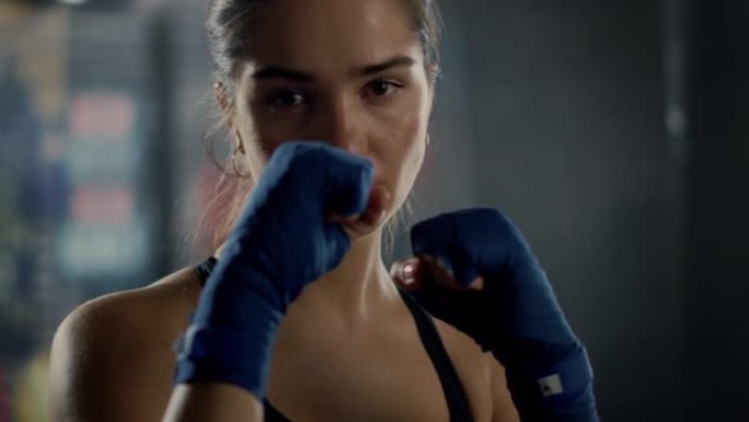 一位美丽健康的黑发跆拳道运动员的肖像在镜头前摆姿势，双手包裹着蓝色的手包。她棕色的眼睛反映了自信和决