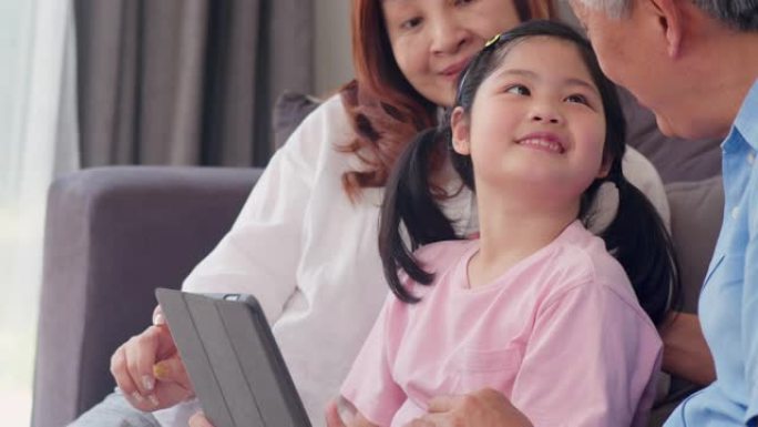 亚洲祖父母和孙女在家里使用平板电脑。中国老年人，爷爷和奶奶快乐度过家庭与年轻女孩一起放松社交媒体，躺